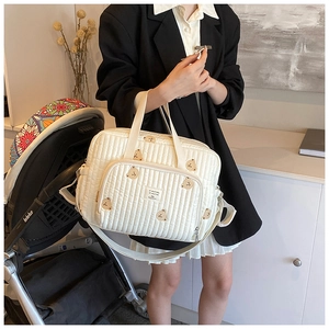 Detail of white quilted diaper bag featuring cute brown bear embroidery and hand strap
