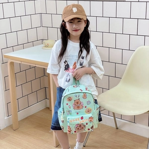 Light green Capybara cartoon kids backpack shown held by a child in a natural setting