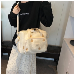 Detailed shot of cream quilted mommy bag featuring cute brown bear embroidery and wide strap