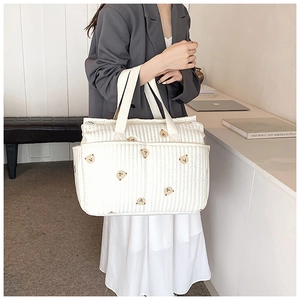 Detail of white quilted diaper bag featuring cute brown bear embroidery and side pockets
