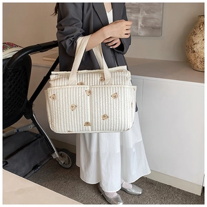 Quilted white diaper bag with brown bear embroidery featuring dual front pockets and large space