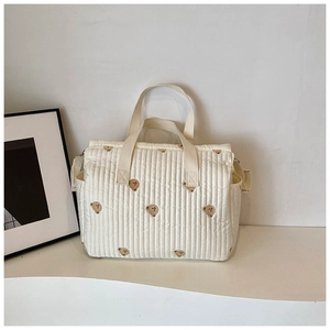 Detail view of the cream-colored quilted diaper bag featuring cute brown bear embroidery