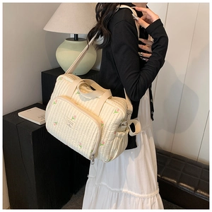 Detail of quilted cotton diaper bag featuring floral embroidery and adjustable strap