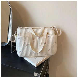 Detailed close-up of quilted floral beige diaper bag with pink embroidery and zipper