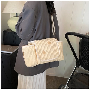 Sac à langer matelassé beige avec broderie ours porté en bandoulière par un mannequin