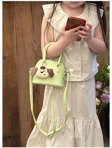 Close-up of mini green kids handbag with cute plush puppy charm and lychee texture