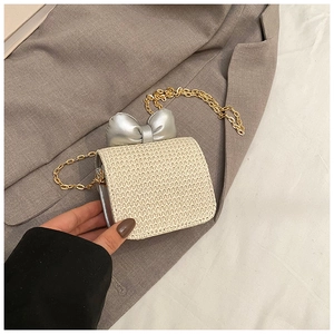Detail of straw woven mini bag featuring a large silver bow and gold chain strap