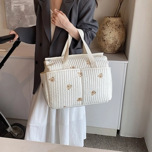 Quilted white tote diaper bag with cute bear embroidery shown in a modern home setting