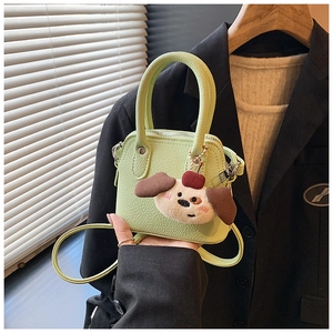 Close-up of pistachio green mini handbag with cute plush puppy charm and textured leather