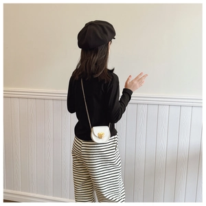 Modèle portant un mini sac bandoulière blanc avec boucle cœur dorée et béret noir