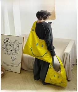 Detail of a large yellow canvas tote bag with a blue smiley face and wide shoulder straps