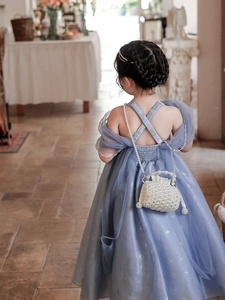 Detailed back view of girl's blue mesh star dress with a woven pearl handle bag