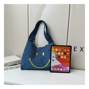 Detail view of blue denim tote bag with yellow smiley face embroidery and iPad for size