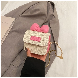 Detail of a mini woven crossbody bag featuring a pink leather bow and gold chain strap