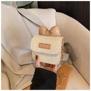 Close-up of woven straw crossbody bag featuring khaki bow and gold chain strap detail