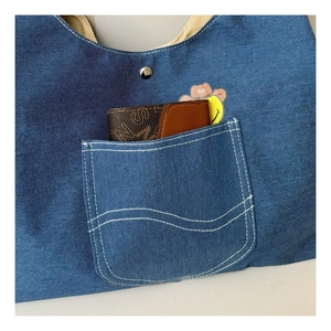 Detail of navy denim crossbody bag with outer pocket showing smile badge and wallet
