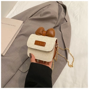 Detail of beige straw crossbody bag with large brown leather bow and gold chain strap
