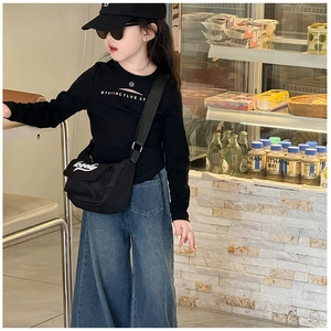 Close-up of children's black crossbody bag with white embroidery on a casual outfit