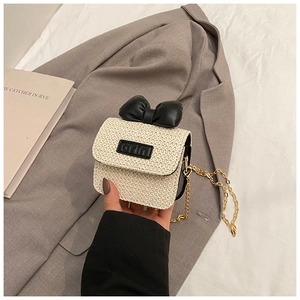 Detail of a beige woven mini bag with a black bow and a golden metal chain strap
