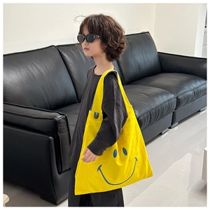Detail of yellow canvas tote bag with blue smiley face print on black leather sofa