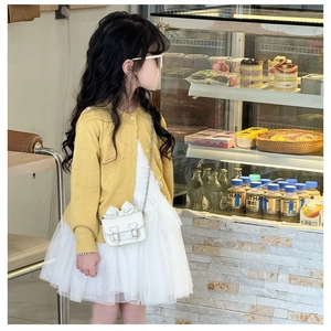 Détail d'un sac à bandoulière blanc à nœud avec chaîne sur un cardigan jaune