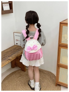 Pink bow kindergarten backpack with striped front pocket shown on a child's back