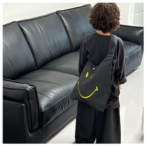 Kids black canvas crossbody bag with yellow smiley face design worn by a model