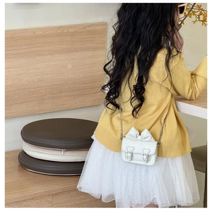Vue arrière d'un enfant portant un mini sac blanc avec un grand nœud et une chaîne