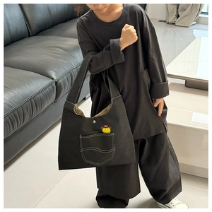 Close-up of black canvas crossbody bag with yellow smiley face patch on a front pocket