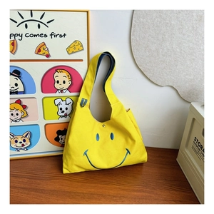 Detail of yellow canvas kids bag featuring blue smiley embroidery and silver magnetic snap
