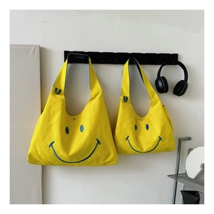 Detail of yellow canvas tote bag set with blue embroidered smiley face and snap closure