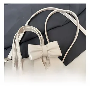 Detail showing comfortable handles and bow decor on cream leather cylinder bag