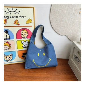 Detail of blue denim shoulder bag featuring a large yellow smiley face embroidery design