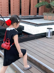 Girl in black dress carrying a red cylindrical bag with bow detail and matching hair tie