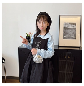 Fille en chemise bleue et robe noire portant un sac à bandoulière matelassé argenté en forme de cœur