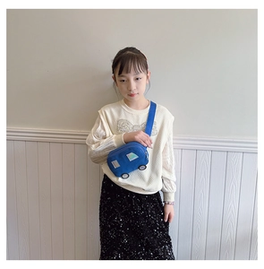 Detail view of a blue car-shaped canvas chest bag worn by a girl over a beige sweater