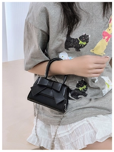 Detail of black mini crossbody bag featuring a large bow and metallic chain strap