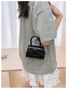 Detail of black mini crossbody bag featuring a cute bow and silver chain strap