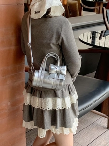 Detail of silver cylindrical girl handbag with metallic bow and adjustable strap