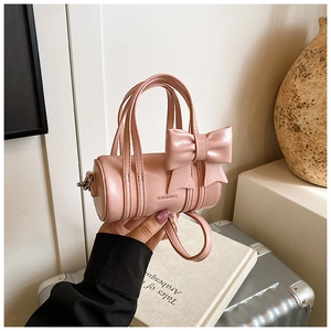 Pink cylinder handbag for girls with a large bow detail and glossy finish being held