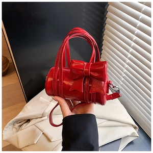 Detail of red cylinder bag with large bow, glossy leather texture, and silver hardware