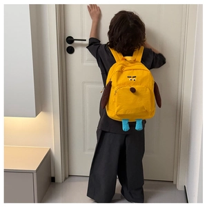 Vista posteriore di un bambino con lo zaino giallo a forma di cane in casa