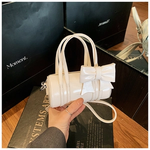 Detail of white glossy patent leather mini cylinder bag for girls with cute bow decoration