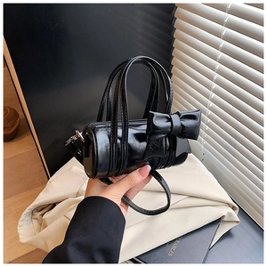 Close-up of black glossy mini cylinder bag with large bow and adjustable strap detail