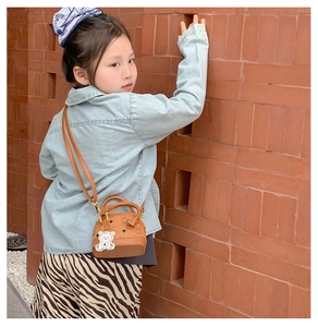 Close-up of brown shell-shaped mini bag with bear charm and laurel leaf print details