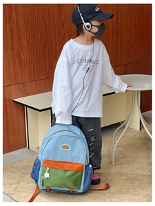 Boy holding a vibrant color-block kids backpack with orange straps and green front pocket