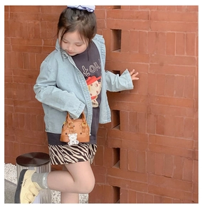 Outdoor lifestyle shot of a child wearing a denim jacket and a brown bear print handbag