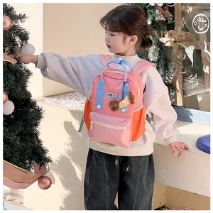 Fille portant un sac à dos scolaire rose et orange avec un pendentif chien en peluche
