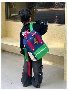 Détail d'un sac à dos enfant tricolore avec panneaux bleu, vert, rouge et ours en peluche