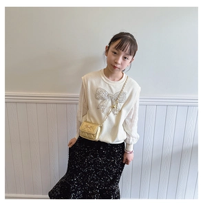 Girl's outfit featuring white knit sweater with sequin bow and gold quilted mini bag